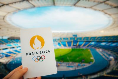 Uma mão segurando um cartão com o símbolo das Olímpiadas de Paris 2024