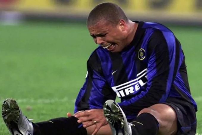 a man sitting on a soRonaldo chorando sentado na gramaccer field with his foot on the ground