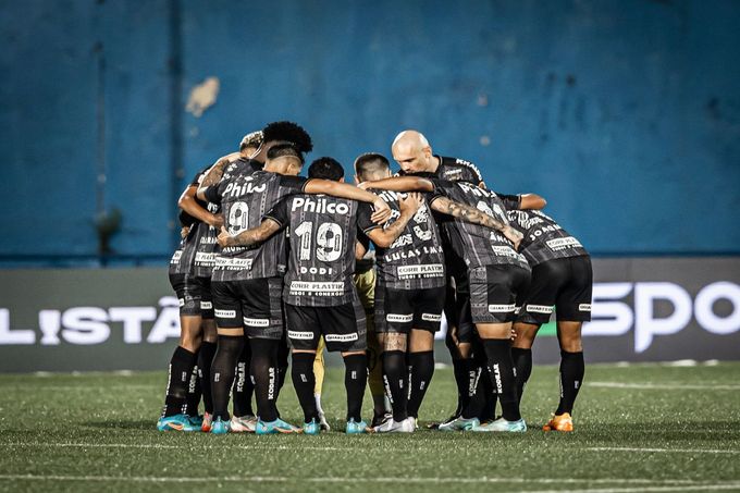 a grupo de jogadores do Santos abraçados, de costas para a câmera, no centro do campo