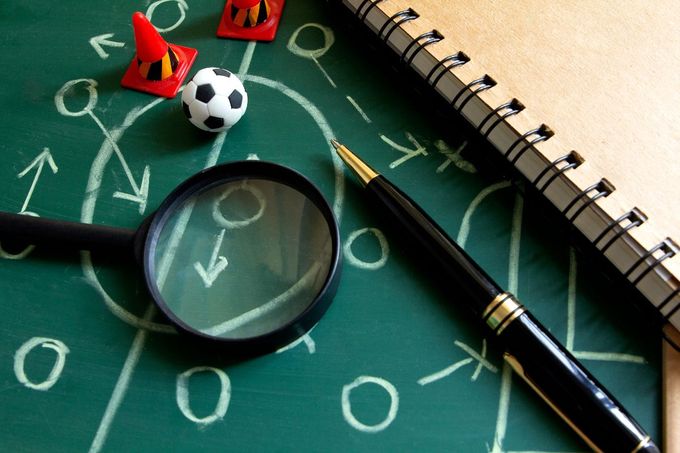 A Uma caneta, um caderno e uma lupa sobre uma superfície verde com estratégias de futebol