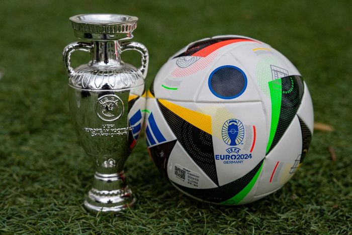 Uma bola de futebol, com o emblema da EURO 2024, ao lado da taça da competição
