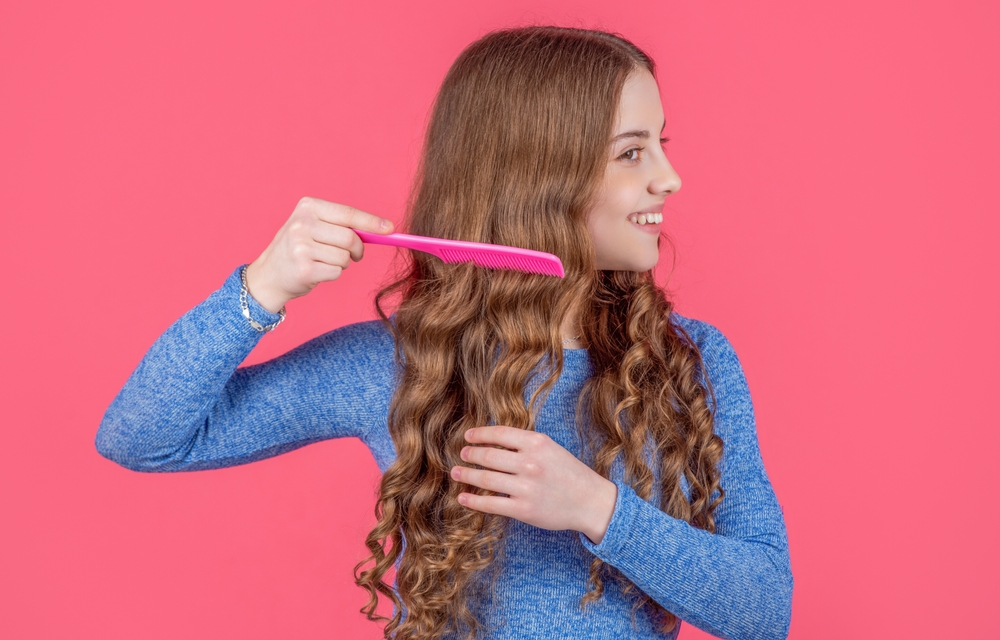 Girl in blue top combing long wavy hair with pink comb
