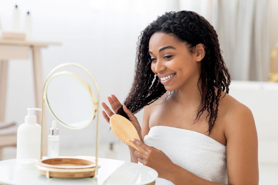 Woman brushing her hair and smiling in front of mirror