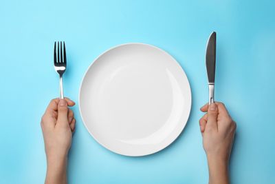 Top view of a person's hands holding cutlery with an empty plate in the middle