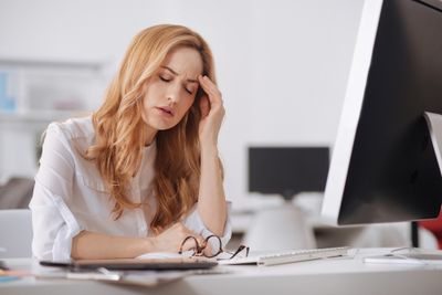 Woman sitting in front of a computer with closed eyes looking exhausted