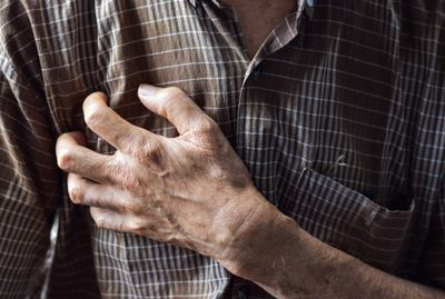 The torso of an elderly person. their arm raised over their chest, hand gripping their heart.