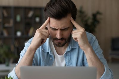 Man looking at his laptop and holding his forehead trying to concentrate