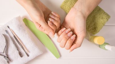 Close-up of woman's hands with long natural nails next to a towel and nail maintenance products