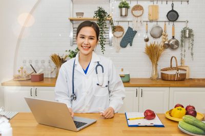 Woman in lab coat standing with laptop in kitchen