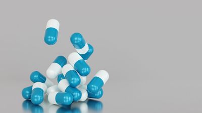A bunch of white-and-blue capsules falling onto a reflect surface, in front of a grey background.
