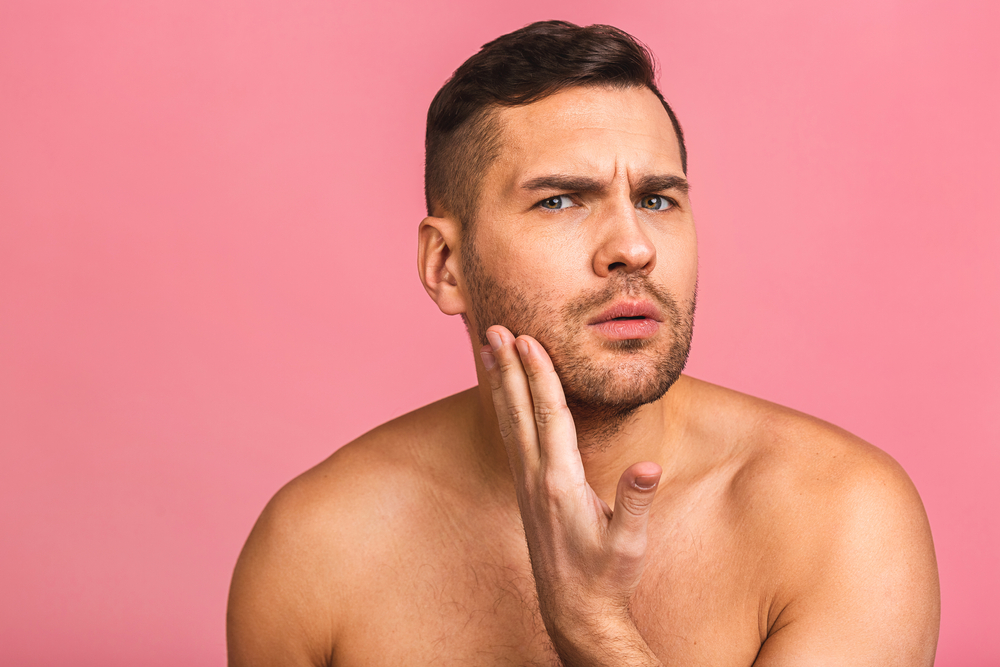 Man touching his face against a pink background