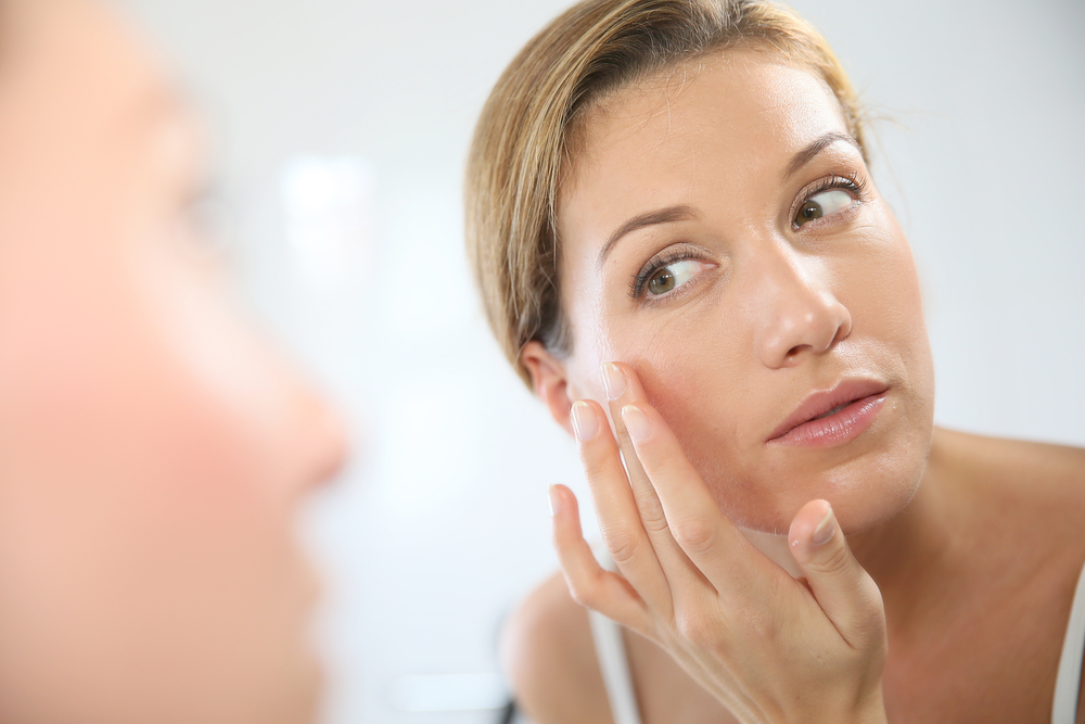 Woman in her 30s looking into the mirror and touching the skin on her face