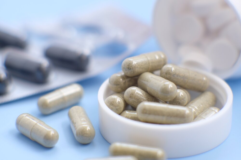 Light brown supplement capsules in the forefront on a cap, with black capsules and white tablets in the background.