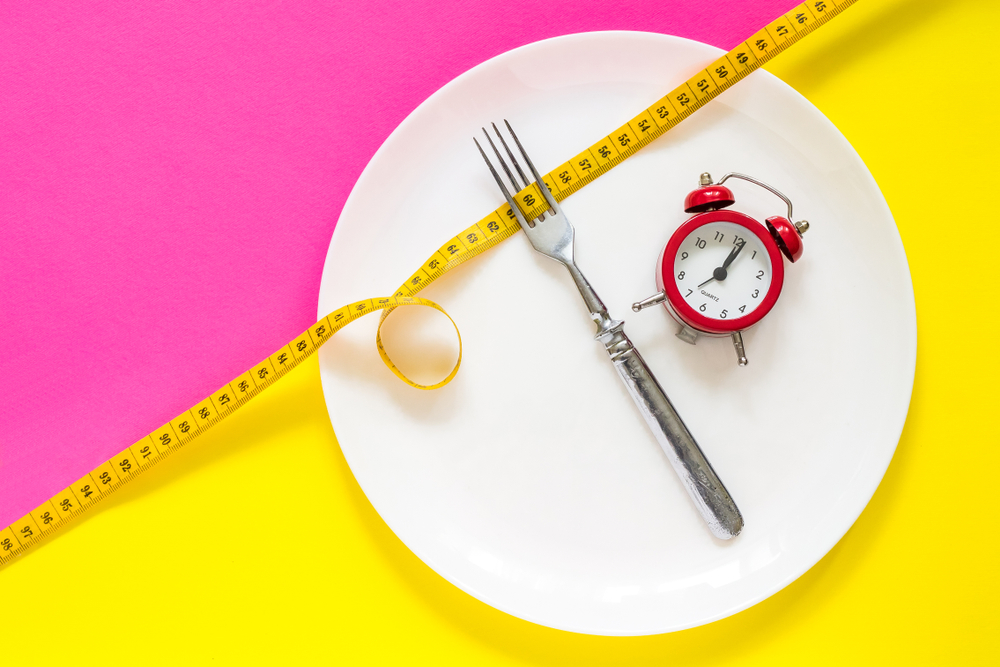 A plate with a fork, clock, and a tape measure on a pink and yellow background