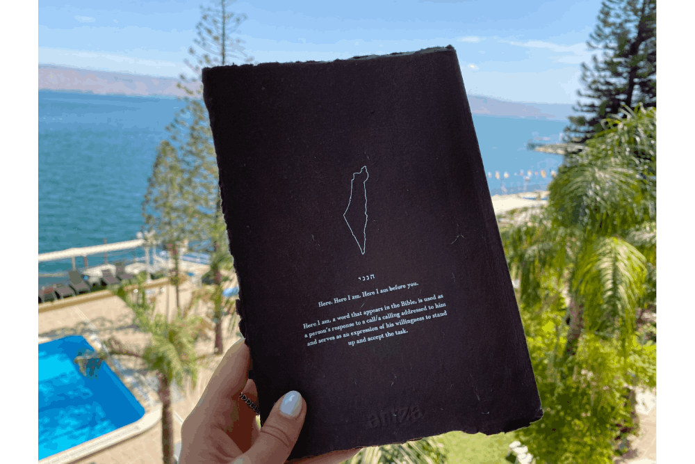 a person holding up a book in front of a body of water