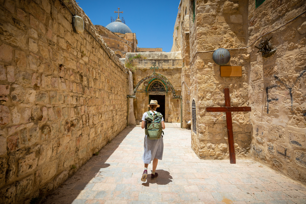 Woman walking in sandstone passageway next to wooden cross