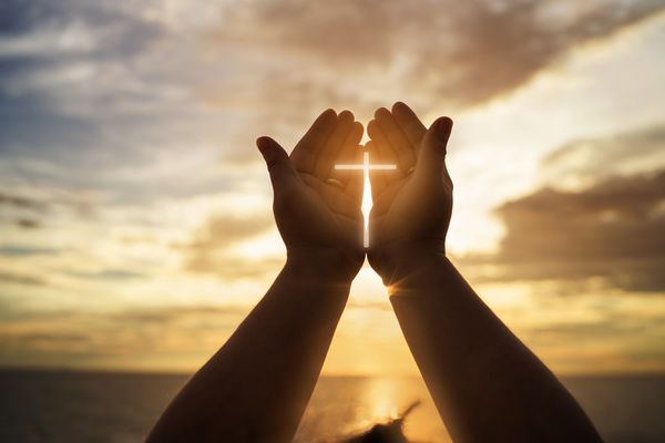 The hands of a Christian holding a cross of shining light 