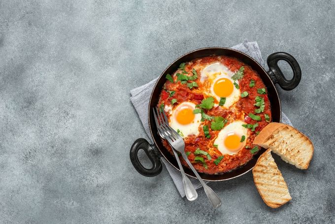 A skillet containing Shakshuka with three eggs and two slices of toast