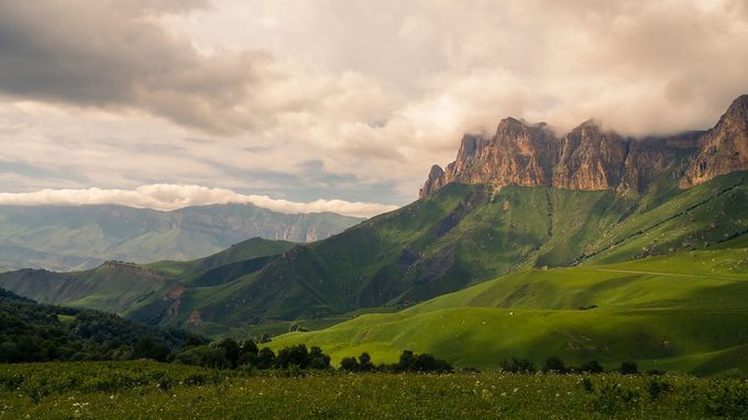 Rocky mountains above green meadows and beneath cloudy sky