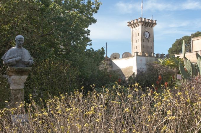 Mount Tabor with clocktower behind stone walls in the background and marble bust of Pope Paul VI