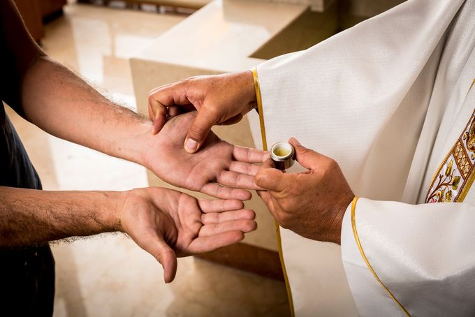 Priest rubbing Christian worshipper's hands with anointing oil