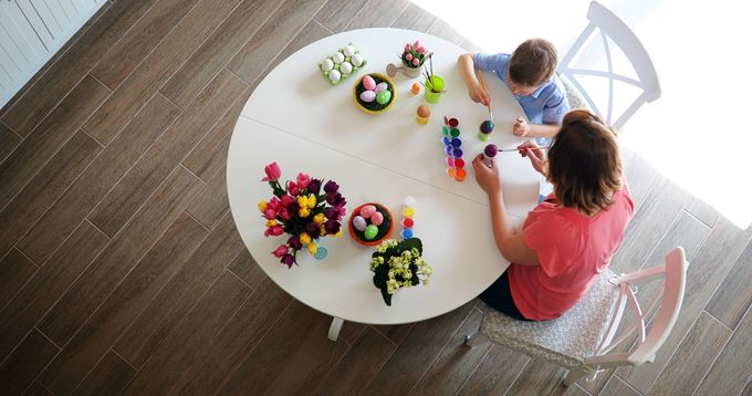 Mother and son painting eggs on white table