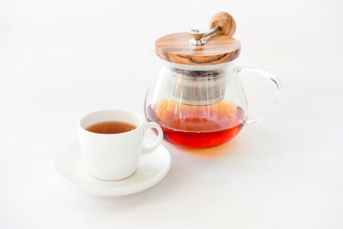 A cup of tea next to a tea pot and saucer.