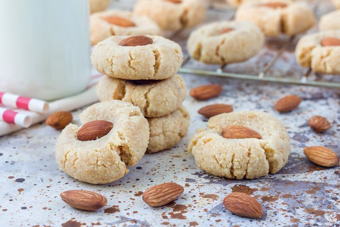 a stack of almond cookies next to a glass of milk