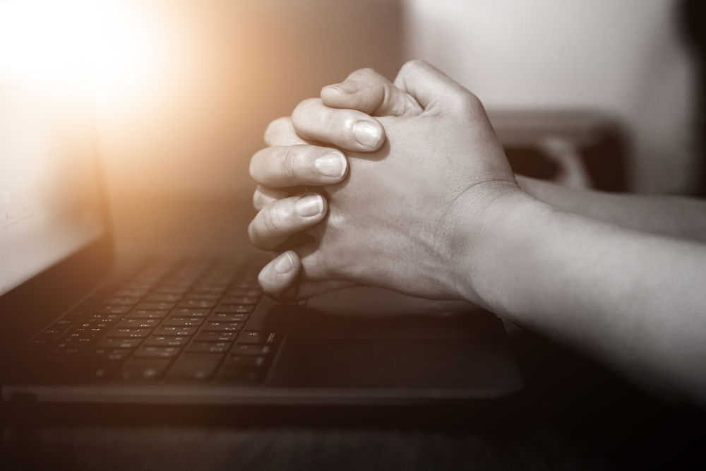 Hands clasped in front of a laptop screen