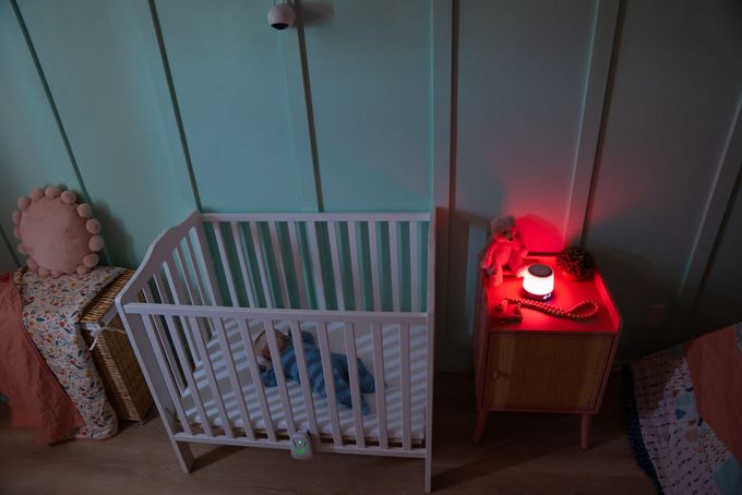 A baby in a crib with a baby monitor on a bedside table.