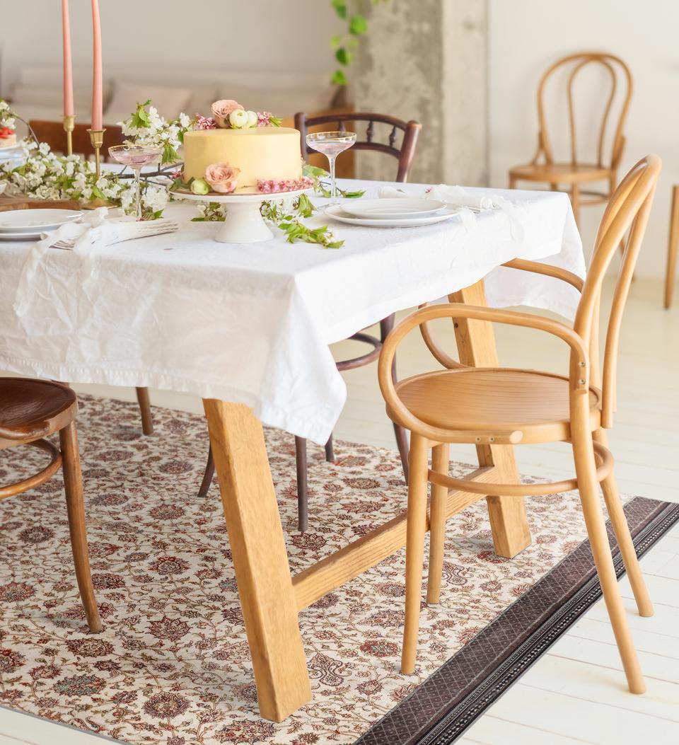 A rug patterned with fall motifs in brown and white tones under a dining room table