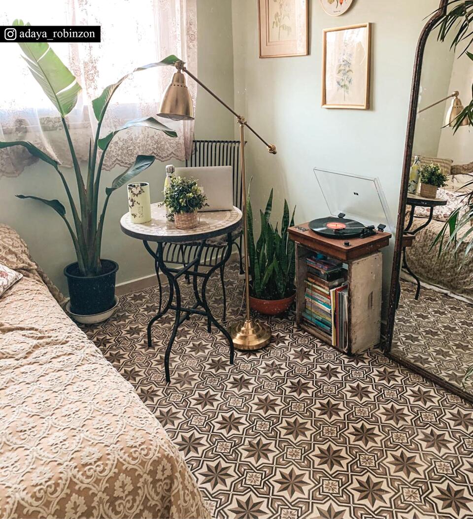 A star-patterned beige and brown rug on the floor of a living room with vintage decor under a coffee table, mirror, and plants