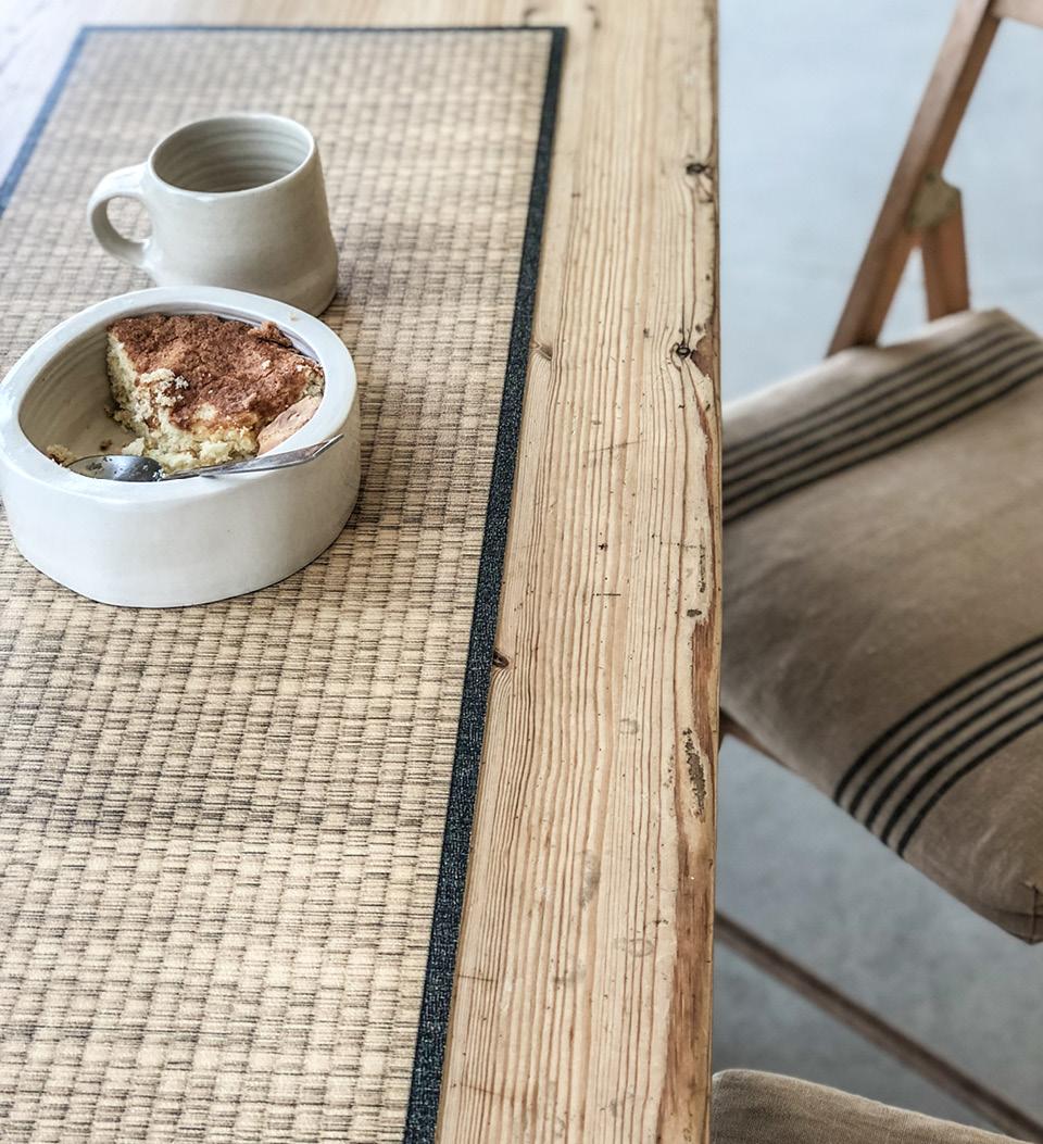 A beige straw-looking table runner on a wooden table under a bowl with food and a cup
