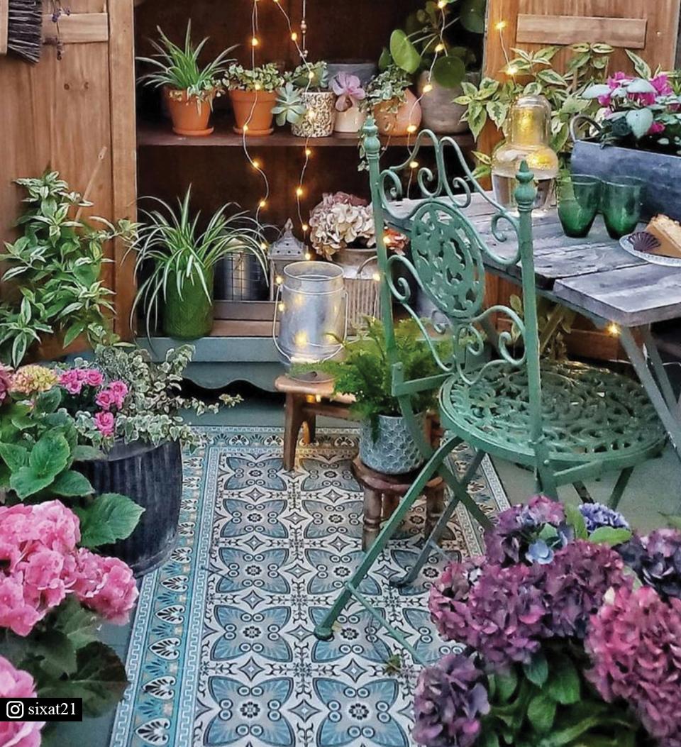 A green floral rug on a patio surrounded by plants and flowers
