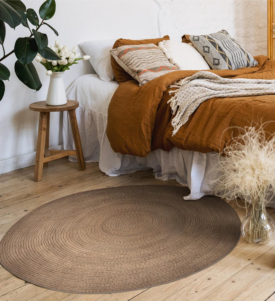 A round woven brown rug on a bedroom floor next to the bed