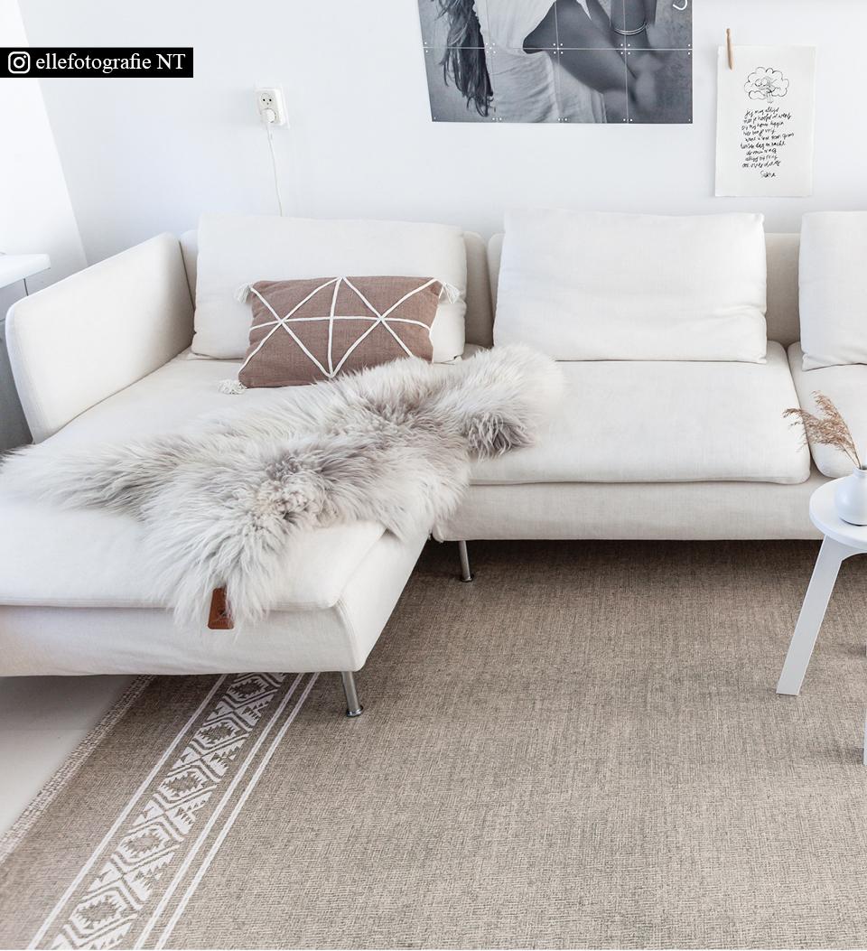 A neutral colored rug with an African traditional pattern on the edges , placed  under an L-shaped living room couch 