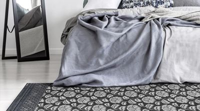 Grey cover over the corner of a bed, with rug on the floor