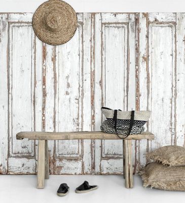 A rustic white wood pannel wall art piece behind a bench with a bag