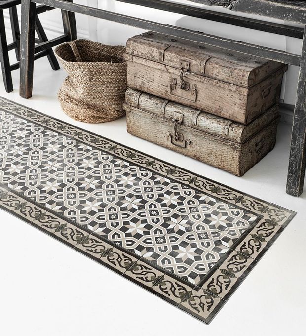 A patterned brown and gray rug on the floor next to a bench and chest decor