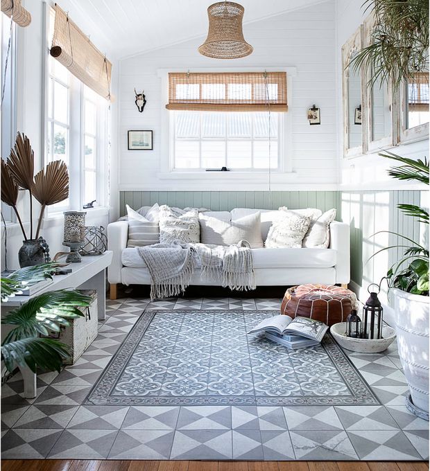 A living room in light tones with a white couch and a patterned rug in subdued green tones