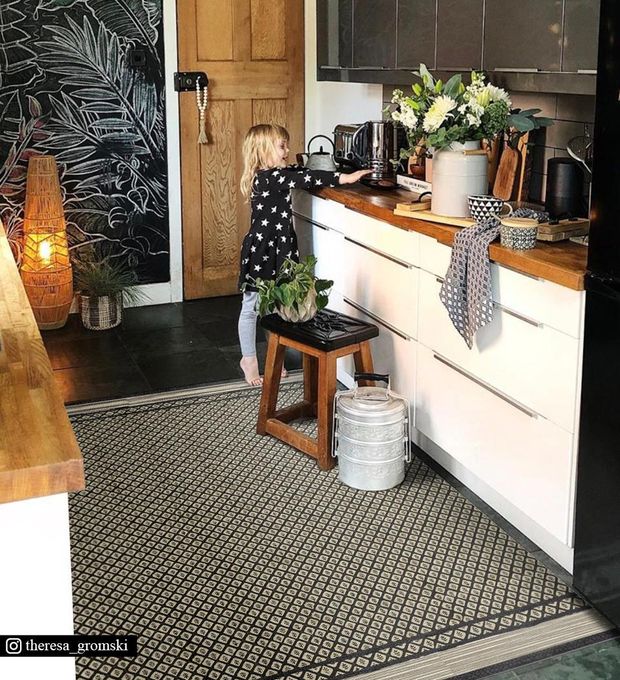 A little girl standing next to the kitchen sink on a black patterned rug