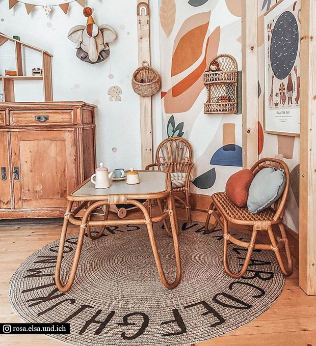 A round braided rug with letters under wicker furniture in a child's playroom