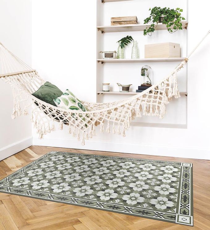 A floral patterned rug in subdued green tones on a living floor under a hammock with pillows in front of a shelf with 