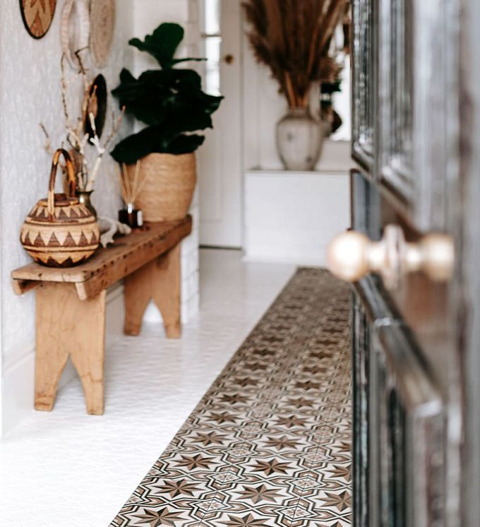 A patterned entryway rug in earthy tones seen through an open front door next to a wooden bench with plants