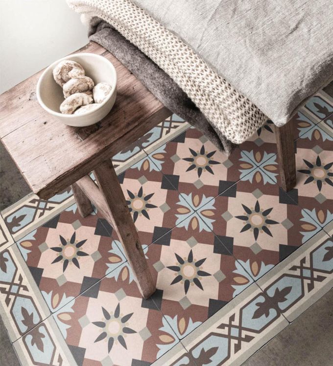 A colorful patterned small rug under a wooden bench with a cookie bowl and folded blankets