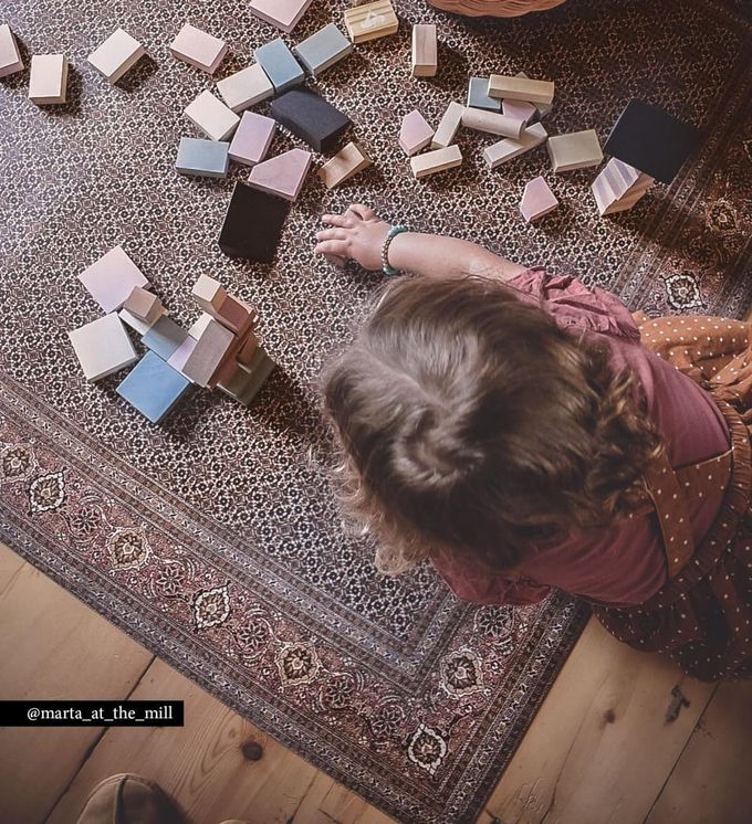A child playing with wooden blocks on a brownish Persian rug