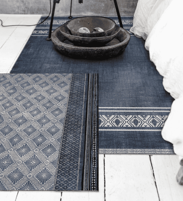 A navy blue rectangle-patterned rug layered over a navy blue solid rug on a white floor