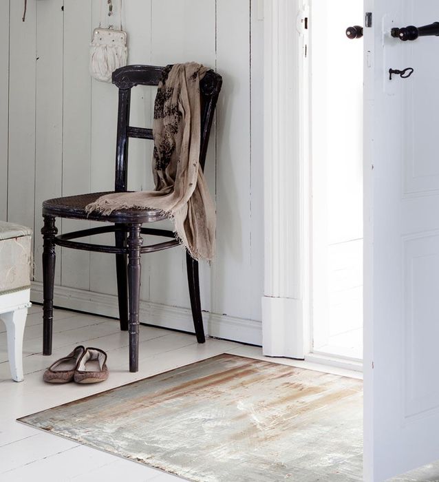 A rusty-patterned rug in a hallway next to an open door, a chair, and slippers