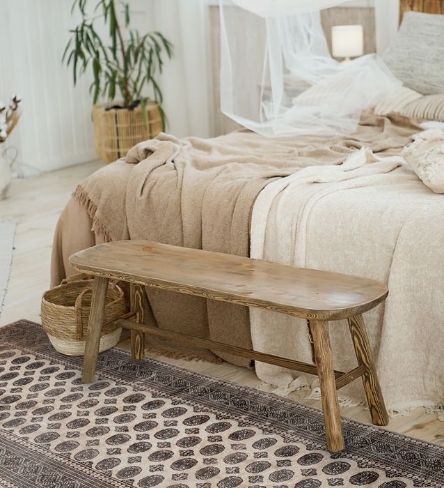 A patterned beige and brown rug on a bedroom floor under a wooden bench