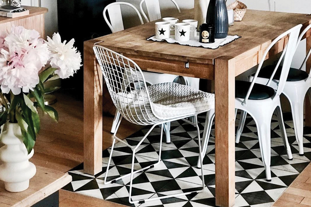 Wooden dining room table with white chairs standing on a monochrome geometric rug